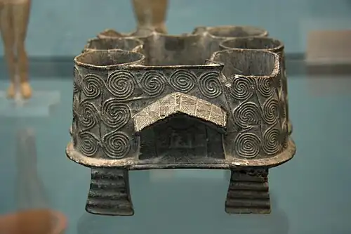 Pyxide multiple en stéatite, de l'île cycladique de Milos (Mélos), Bronze ancien, vers 2500 av. J.-C. Elle se compose de sept vases cylindriques séparés par des cloisons, avec des sculptures évoquant des lieux de culte.