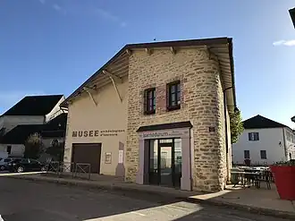 Photographie en couleurs d'une maison avec en façade l'enseigne « musée archéologique d'Izernore ».