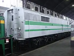 Photo couleur montrant l'arrière d'une loco blanche à bande verte. Une porte permet la circulation avec le train, mais il n'y a pas de vitre de cabine.