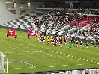 Photographie en couleur d'un terrain de football où deux équipes font leur entrée.