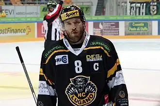 Photographie couleur d’un hockeyeur, de face, en buste, la tête légèrement penchée sur sa droite.