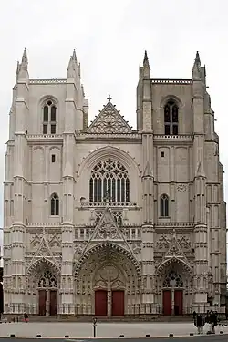 Façade : deux tours carrées encadrent la nef, bâtiment de style gothique en tuffeau blanc.