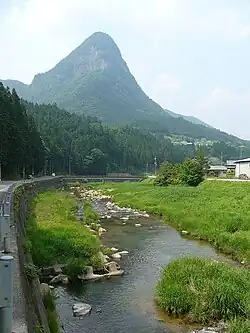 Photo couleur d'un cours d'eau avec en arrière-plan une montagne sous un ciel bleu et nuageux.
