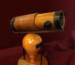 Un télescope en bois est monté sur une sphère et un socle de même.