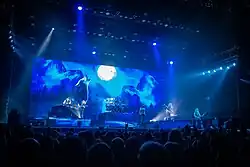 image d'un groupe de rock jouant devant un écran montrant un loup hurlant à la lune