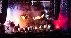 Quatre membres d'un groupe de rock jouant sur une scène avec des effets pyrotechniques