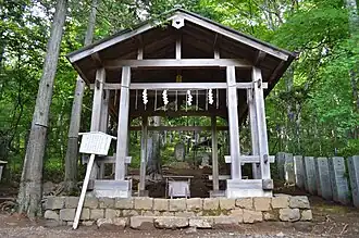 Photo couleur d'un hall ouvert en bois gris, entouré d'arbres.