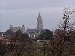 Photographie en couleur représentant un terrain vague dans le quartier de Banzeau, avec à l'horizon les tours de l'église Saint-Philbert et du château de Noirmoutier.