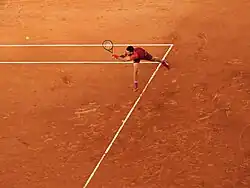 Photo de Novak Djokovic frappant un revers, sur fond de terre battue.