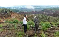 Photographie de deux hommes debout devant un paysage de collines déboisées.