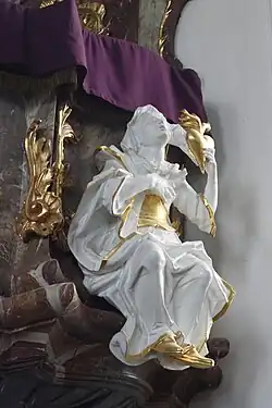 Vue de gauche, statue d'un jeune homme drapé de blanc avec parures d'or, bras droit levé vers le ciel, accroché à la chaire de l'église.