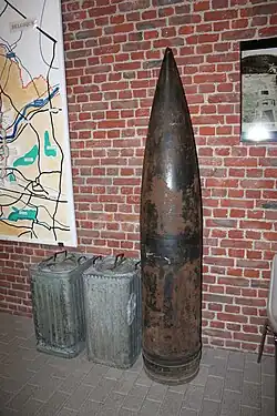 photographie prise dans un musée montrant un obus de la taille d'un homme devant un mur de briques.