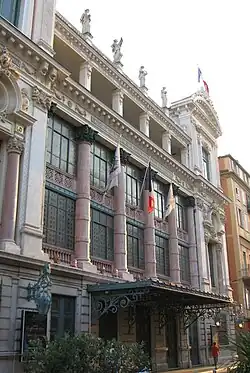 Vue d'un bâtiment de style italien du XVIIIe&nbsp;siècle à colonnes et grandes baies vitrées et statues sur son toit plat.