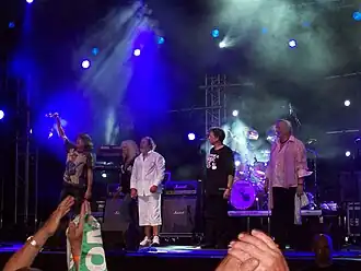 Scène de concert avec quatre hommes et une femme sur la scène devant une foule.