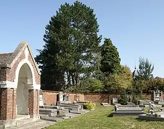 Cimetière, avec à gauche le calvaire. Remarquer à l’arrière-plan à droite, émergeant de derrière les arbres, le bulbe à flèche du colombier seigneurial.