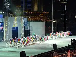 Photo d'une scène éclairée montrant des personnes portant des drapeaux, au fond des immeubles