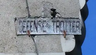 Panneau scellé dans un mur et portant l'inscription « DÉFENSE DE TROTTER ».
