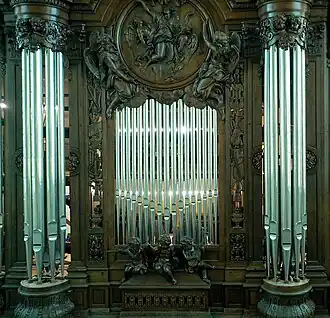 Plate-face d'un grand buffet d'orgue en bois, avec trois statues d'angelots musiciens au bas de l'image, deux tourelles à droite et à gauche et, en haut de l'image, un médaillon d'un homme entouré d'anges.