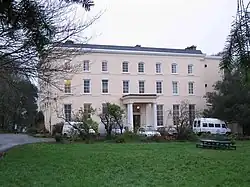 Photo d'un bâtiment rectangulaire de trois étages à la façade saumon, avec de nombreuses fenêtres. L'entrée est sous un porche soutenu par quatre colonnes blanches