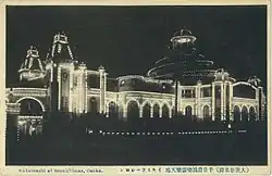 Derrière une façade d'immeubles se détache en arrière plan la structure illuminée en forme de dôme d'une salle de spectacle (image en noir et blanc).