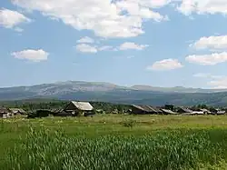 Paysage de montagne, quelques maisons de bois et un massif modéré au loin.