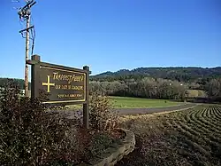 Photographie couleur du panneau annonçant l'entrée d'un monastère dans un paysage rural