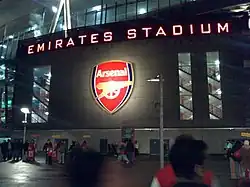 Photo de l'entrée du stade de nuit avec « Emirates Stadium » en majuscules éclairées sur la façade.
