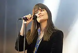 Chanteuse souriante en plan poitrine, devant un micro sur pied.