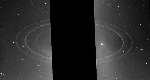 Image éloignée de la planète, trois grands anneaux sont visibles et la planète cachée par une bande noire.