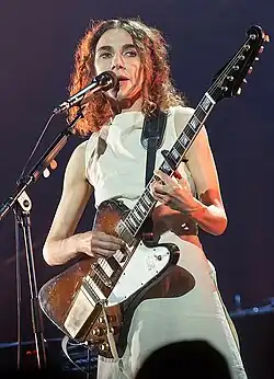 Image d'une femme brune habillée de blanc jouant de la guitare électrique