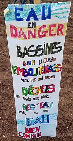 Une pancarte en bois blanche, plantée dans un champ labouré, sur laquelle sont écrits en couleur différents slogans anti-bassines