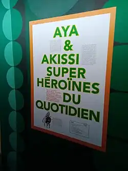 Panneau à l'entrée de l'exposition Aya et Akissi (BDFIL, 2024) : en lettres majuscules vertes on peut lire Aya et Akissi super héroïnes du quotidien.