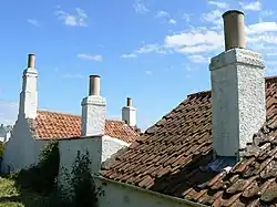 Des toits de tuile d'où sortent des souches de cheminée.