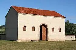Restitution d'un bâtiment antique avec grande porte, petites fenêtres et toiture tuiles.