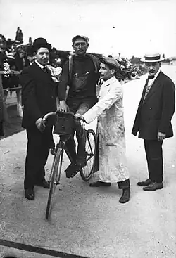 Photographie noir et blanc d'un cycliste entouré de quelques personnes debout.