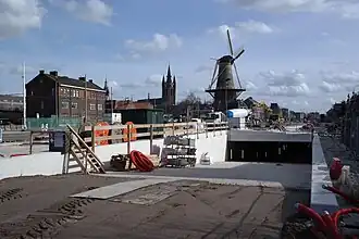 Photographie en couleurs d'un moulin à vent entouré d'un paysage urbain en travaux.