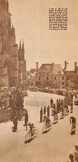 Photo en noir et blanc d'un groupe de cyclistes passant dans un village avec une église dans le fond de l'image.