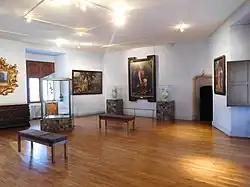Photographie en couleur d'une salle d'exposition avec des tableaux et des objets d'art.