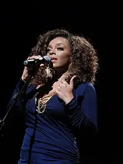 Portrait mi-hauteur en couleur d'une chanteuse. De sa main droite elle tient un micro.