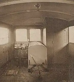 Photographie en sépia d'un poste de conduite de train à gauche avec un capot moteur au milieu et un cabinet de toilette à droite.