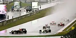 Photo de plusieurs monoplaces de Formule 1 roulant sous la pluie, à l'approche d'un virage