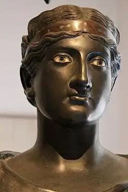 L'une des 5 péplophores (vêtues d'un péplos). Plusieurs semblent s'habiller. Celle-ci porte un bandeau dans les cheveux, composé de plusieurs métaux, choisis pour leurs couleurs.