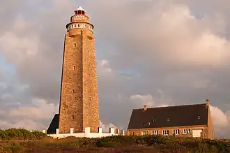 Photographie en couleurs prise d'assez près vers un phare bordé par un bâtiment.
