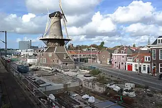 Photographie en couleurs d'un moulin à vent entouré d'un paysage urbain en travaux.