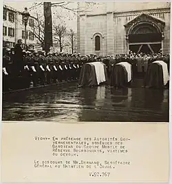 Photo noir et blanc (avec une légende) : au centre trois cercueils recouverts d'un drapeau, à gauche des hommes en uniforme avec casques et gants blancs, au fond des officiels.