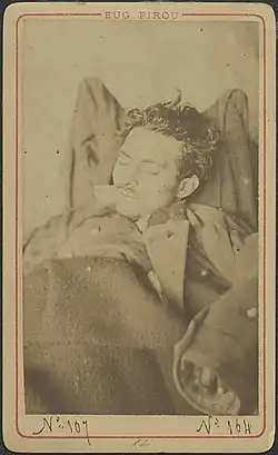 Photographie sépia du cadavre d'un homme jeune, portant une légère moustache, les yeux clos.