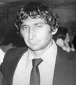 Photographie en noir et blanc du buste d'un homme portant une chemise blanche, une cravate noire et une veste noire