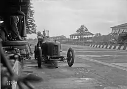 Photo d'une voiture immobilisée en bord de piste pour un ravitaillement (opéré avec un seau).