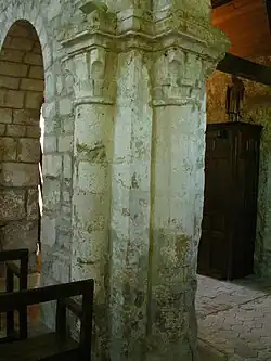 Piliers accolés à une arche ; deux chapiteaux ornés de motifs végétaux sont visibles.