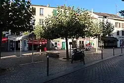 Photographie d'une place ombragée avec des maisons en arrière-plan.